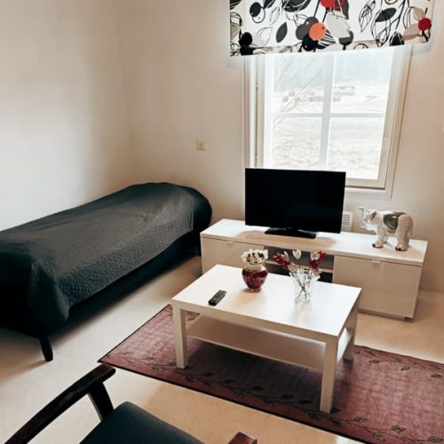 Asukashuone, jossa on sänky, televisio ja pieni pöytä